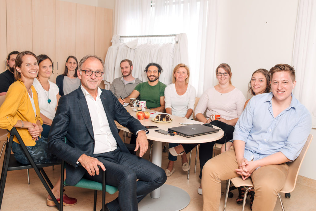 Gruppenbild: das gesamte Team an einem Tisch, links vorne der ärztliche Leiter Dr. Hans Haltmayer