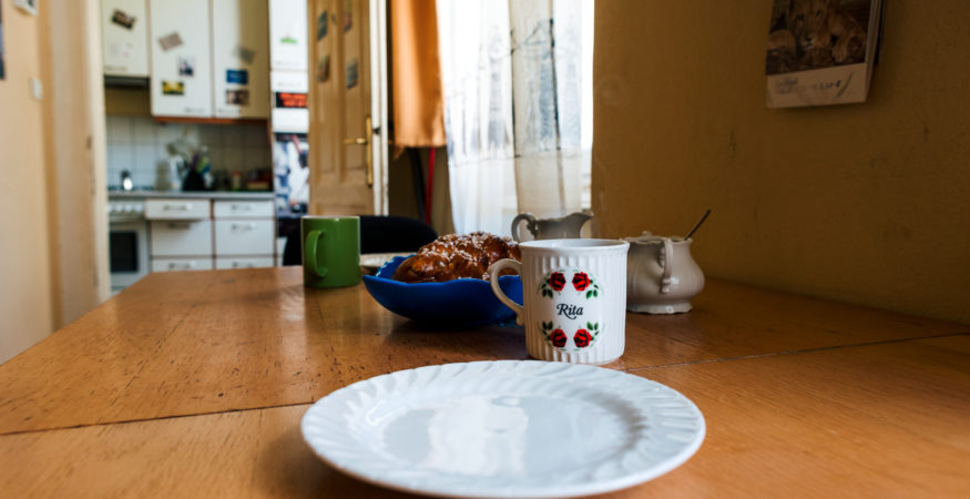 Close-Up auf gedeckten Frühstückstisch, im Hintergrund ein Fenster und die Küche