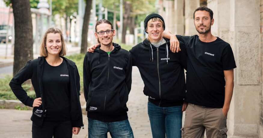 Team-Porträt: 4 Kolleg*innen in schwarzen T-/Sweat-Shirts mit weißem Aufdruck "streetwork" auf der Brust