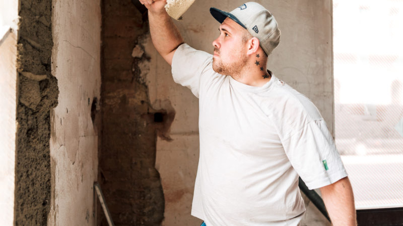 Seitenansicht: Bauarbeiter holt Schwung mit der Maurerkelle beim Verputzen einer Wand