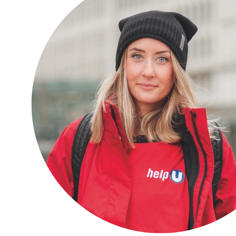 Portrait von einer help U MItarbeiterin mit roter Jacke und Mütze, auf der linken Brustseite ist das help U Logo abgebildet.