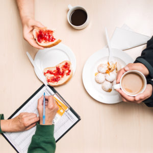 Besprechung beim Frühstück – Kaffeetasse, Marmeladebrote, ein Klemmbrett, auf das notiert wird