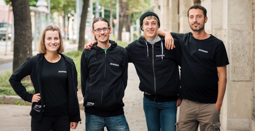 Team-Porträt: 4 Kolleg*innen in schwarzen T-/Sweat-Shirts mit weißem Aufdruck "streetwork" auf der Brust