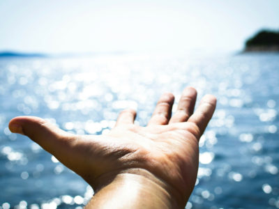 Symbolbild für Leben ohne Drogen: geöffnete, sonnenbeschienene Hand, die sich nach dem Meer streckt
