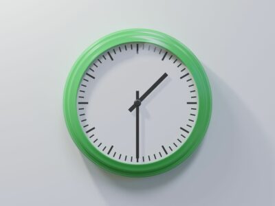 Uhr mit grüner Umrandung hängt an der Wand. Die Zeiger zeigen 13:30 Uhr